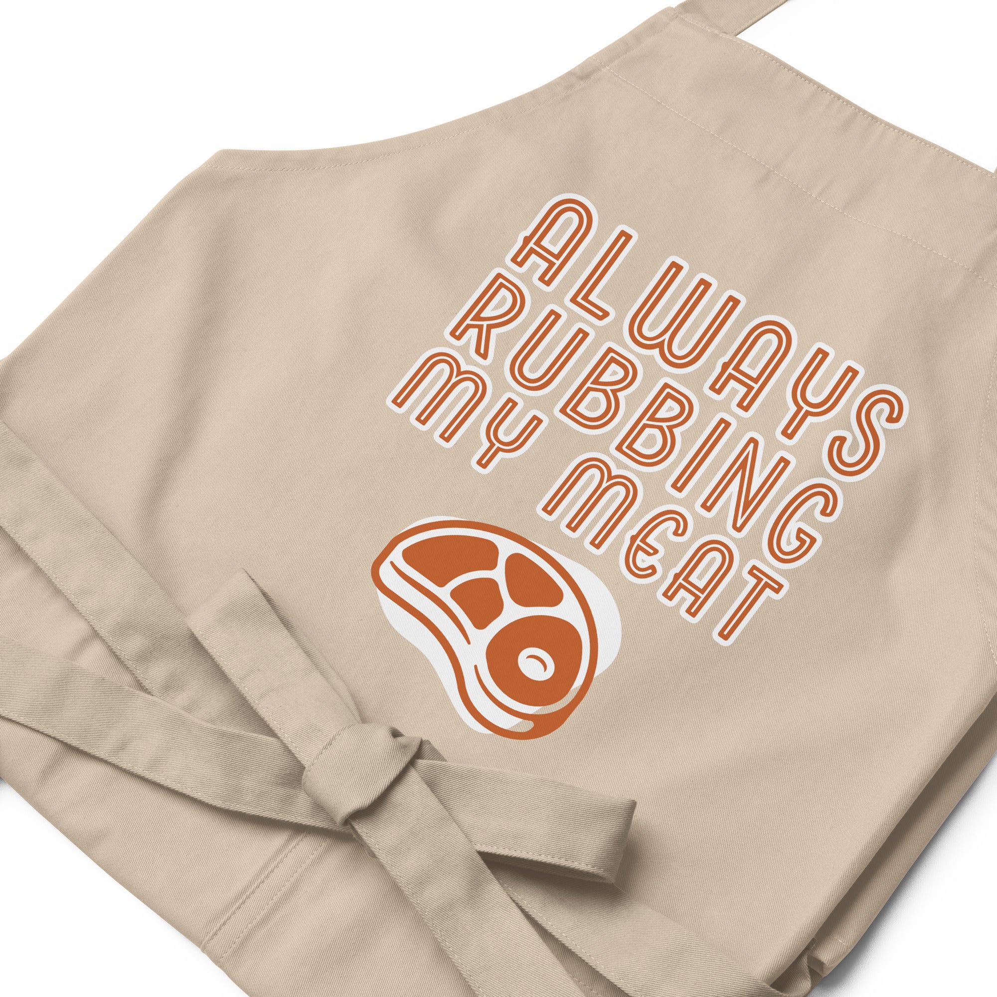 Beige grilling apron with an illustration of a steak with the caption "Always rubbing my meat."